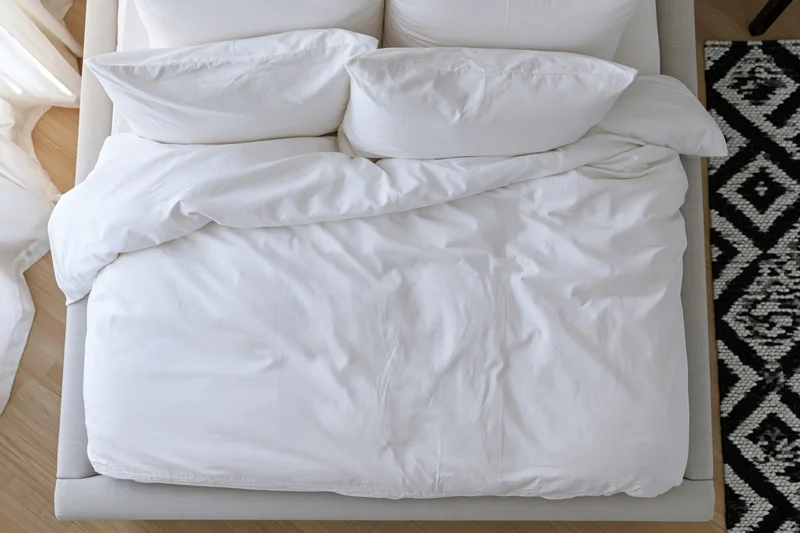 Overhead view of a neatly made bed with white cotton bedding in a modern bedroom