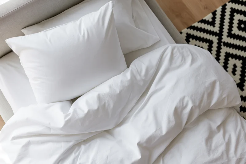 Overhead view of rumpled white cotton bedding on a bed in a bedroom