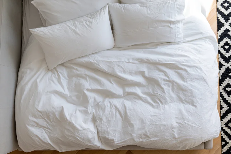Overhead view of a rumpled white cotton bed with pillows in a bedroom