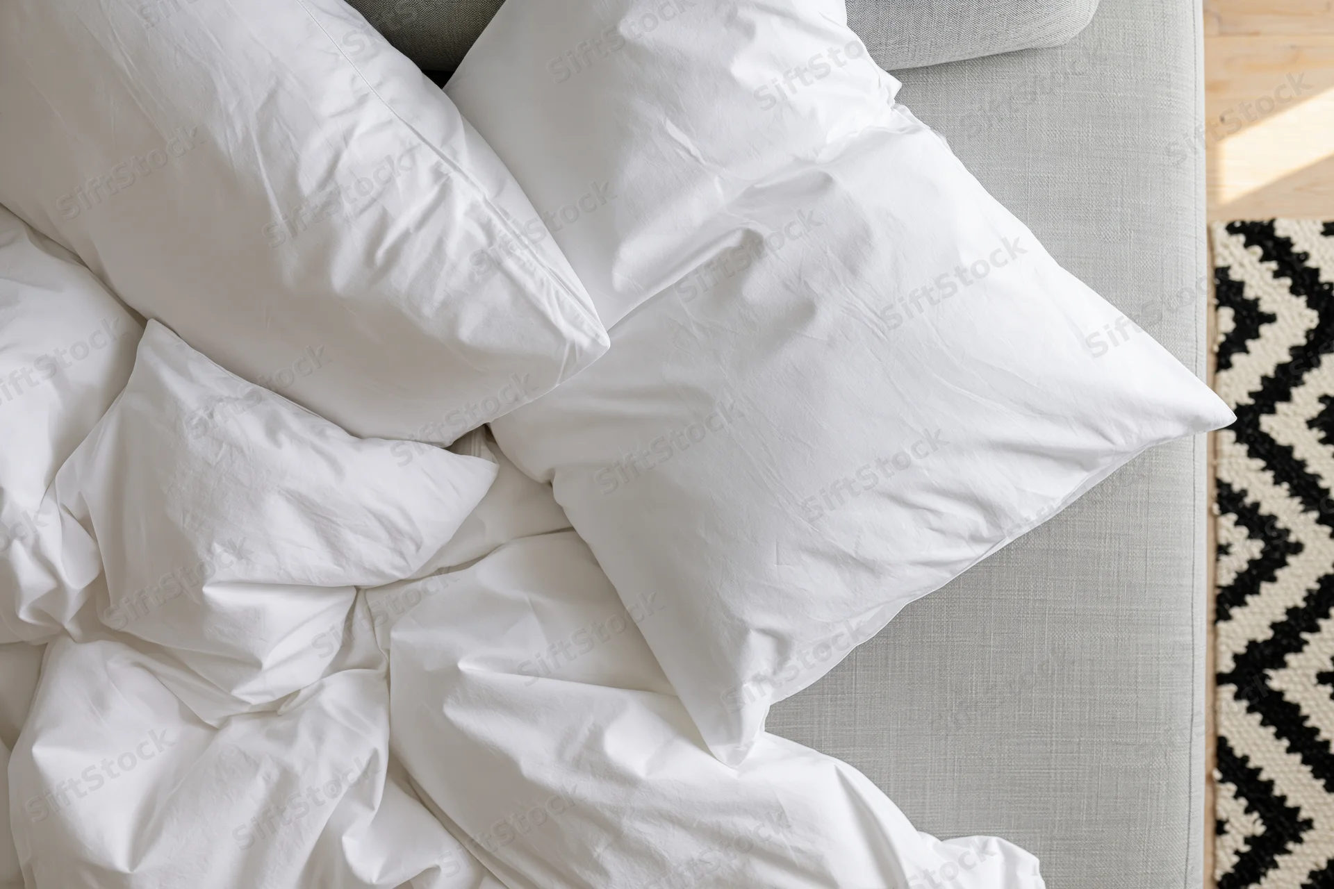 Crumpled white cotton bedding and pillows on a gray sofa beside a black and white patterned rug
