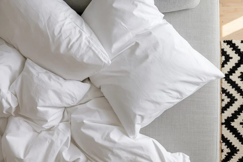 Crumpled white cotton bedding and pillows on a gray sofa beside a black and white patterned rug