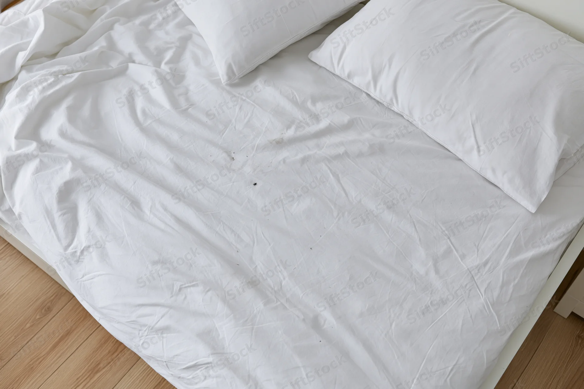 Overhead view of unmade bed with white cotton sheets and pillows on wooden floor