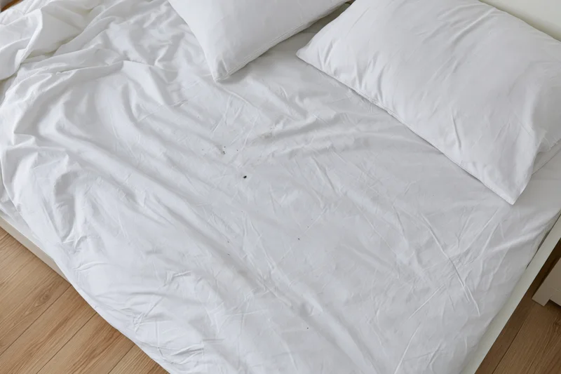 Overhead view of unmade bed with white cotton sheets and pillows on wooden floor