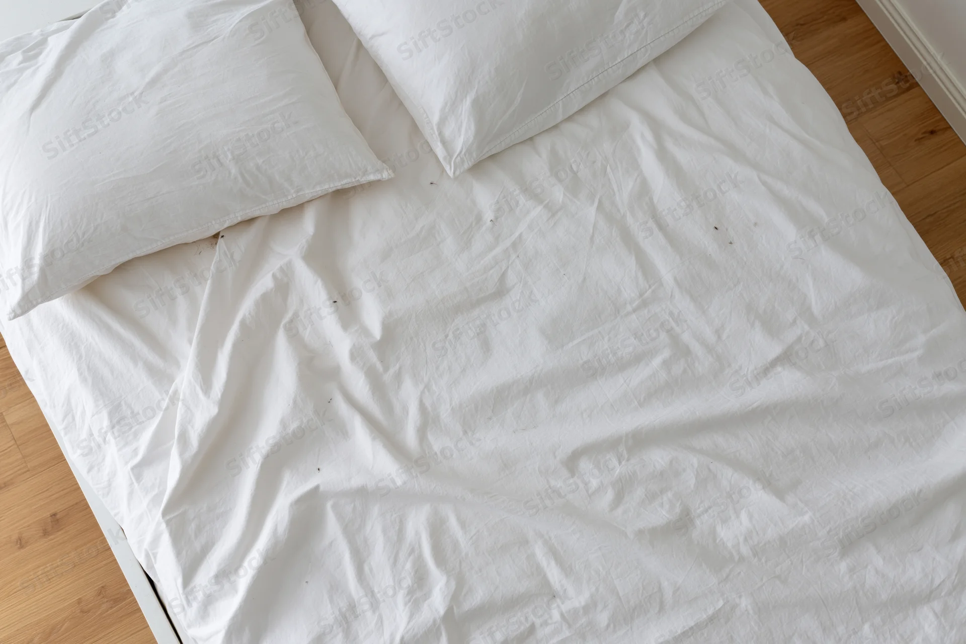 Unmade bed with white cotton sheets and pillows on wooden floor