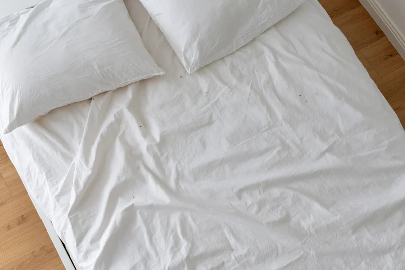 Unmade bed with white cotton sheets and pillows on wooden floor