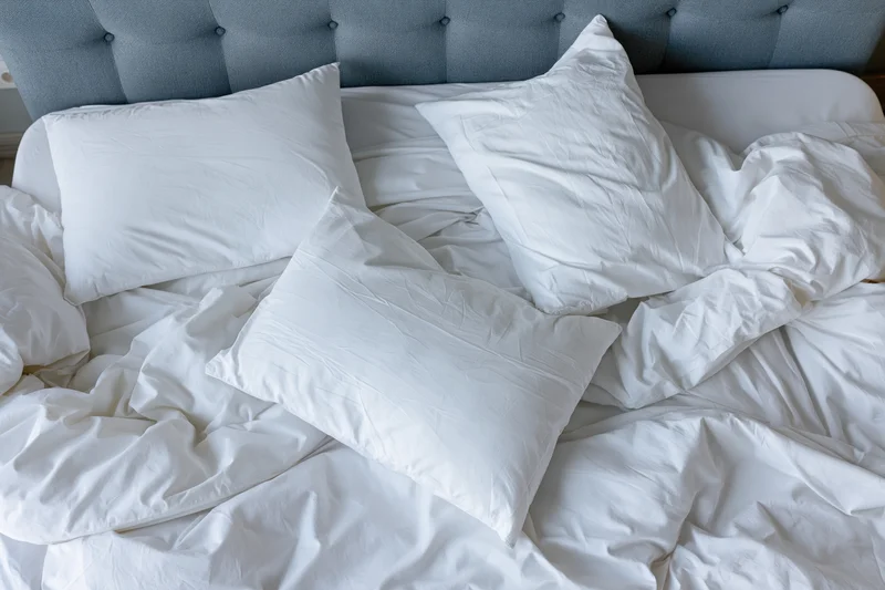Unmade bed with white cotton pillows and crumpled sheets against a tufted headboard
