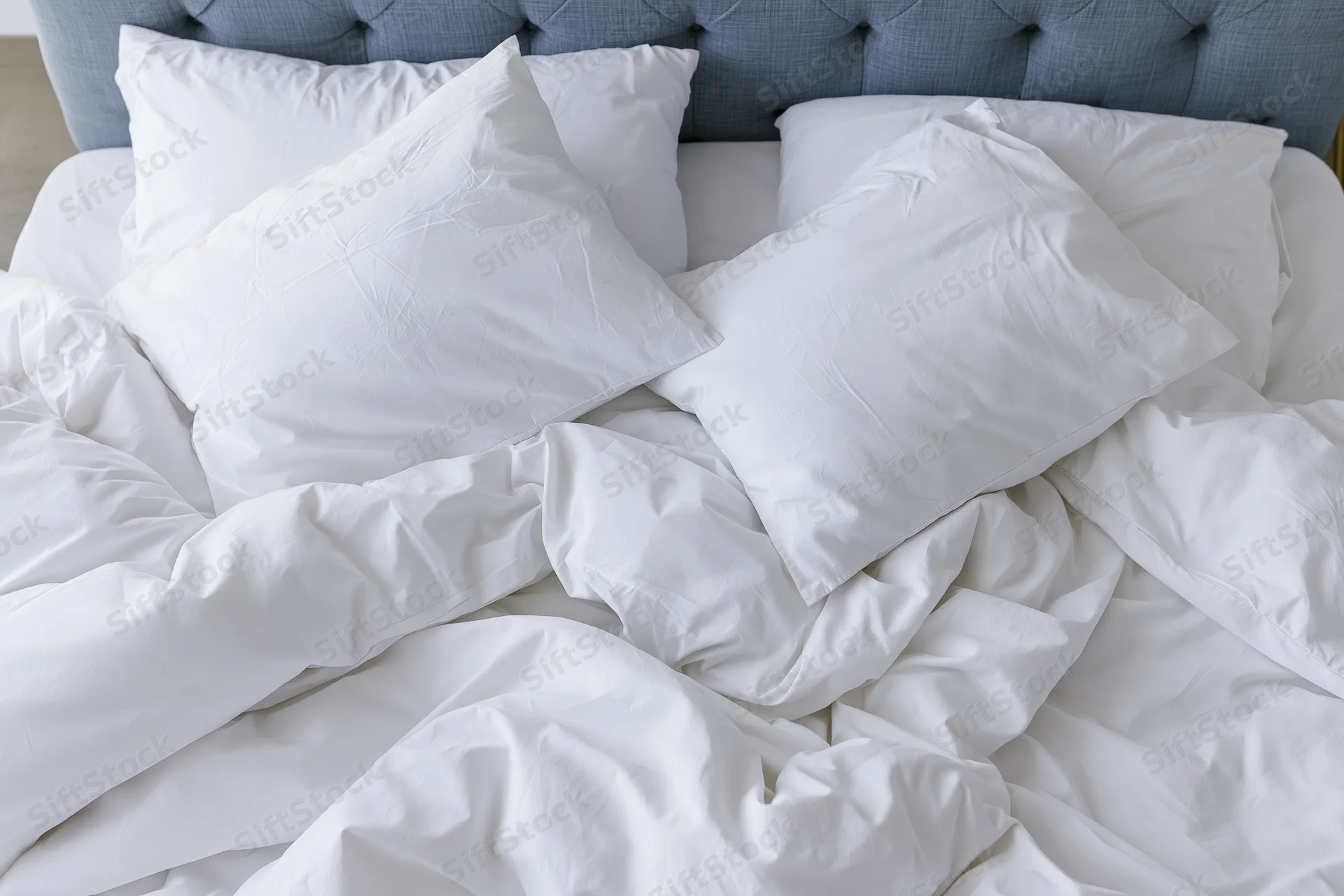 Unmade bed with white cotton pillows and crumpled sheets, viewed from above, against a tufted headboard