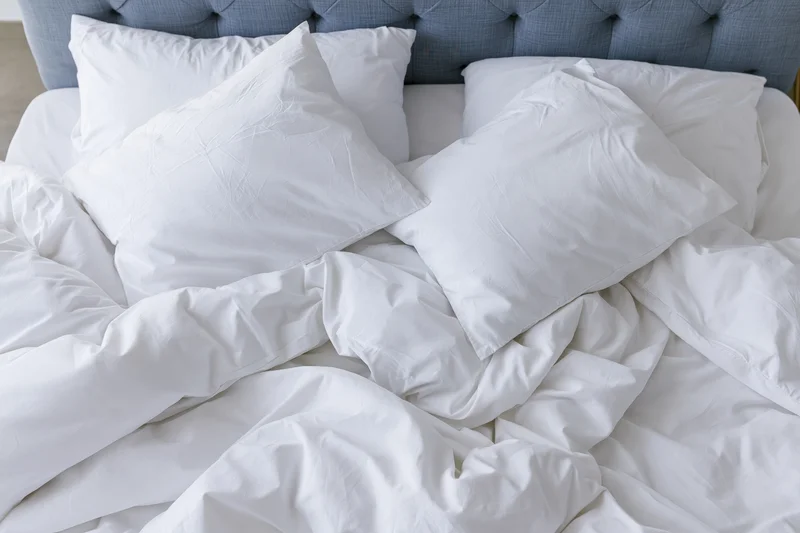 Unmade bed with white cotton pillows and crumpled sheets, viewed from above, against a tufted headboard