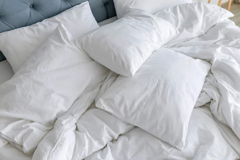 Unmade bed with white cotton pillows and crumpled bedding in a bedroom