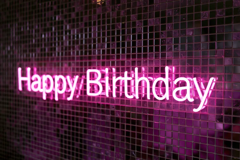 Pink neon happy birthday sign glowing on a mosaic tile wall