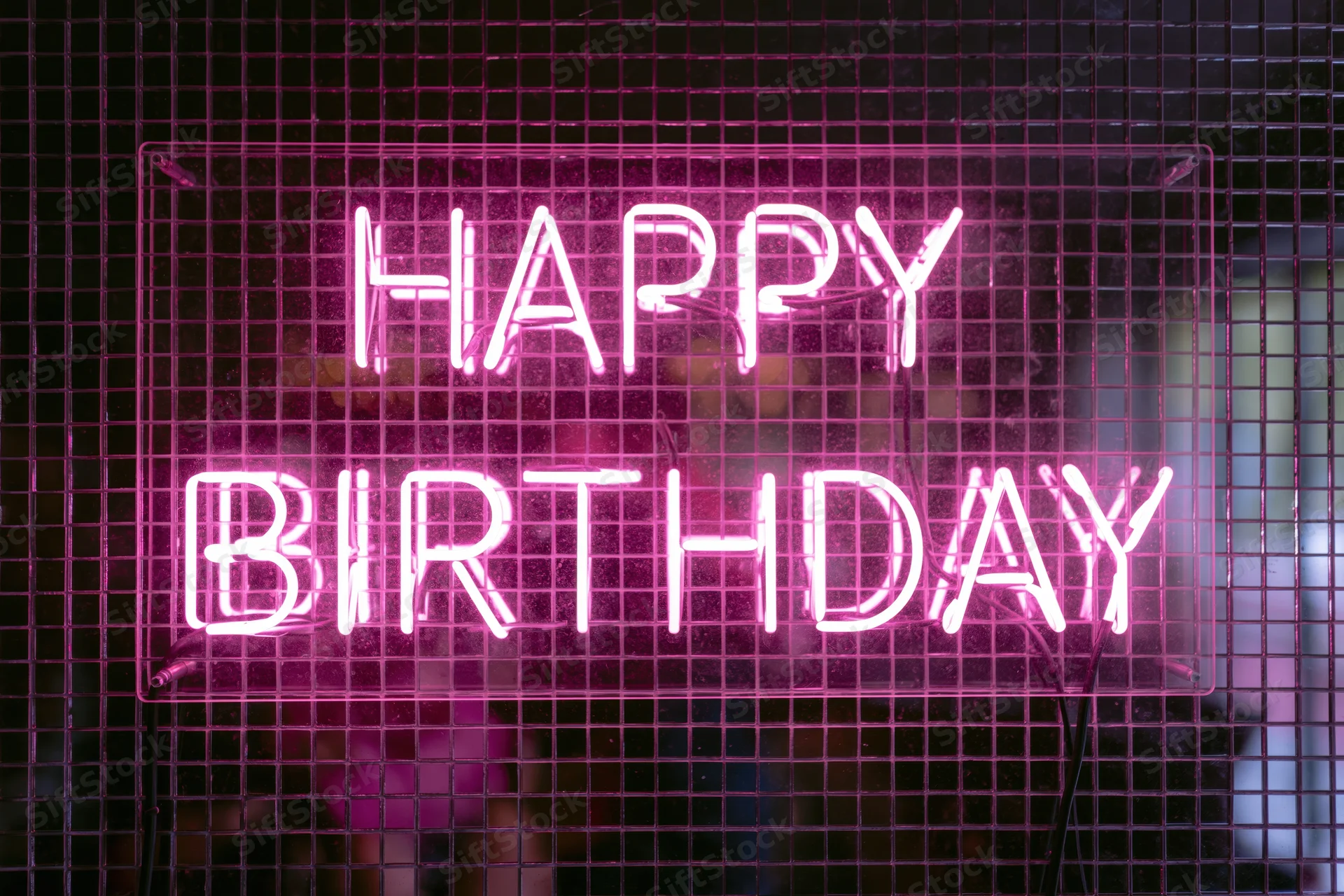 Pink neon happy birthday sign mounted on a metal grid wall