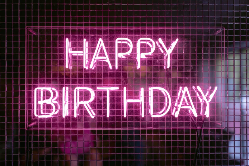 Pink neon happy birthday sign mounted on a metal grid wall