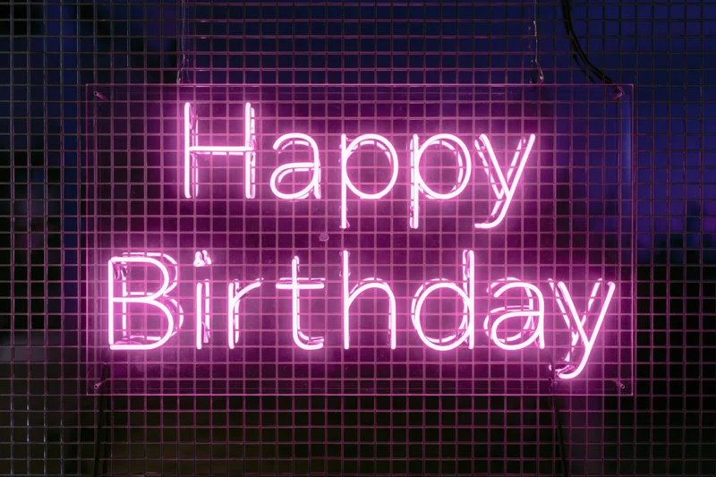Pink neon happy birthday sign mounted on a metal grid wall at night