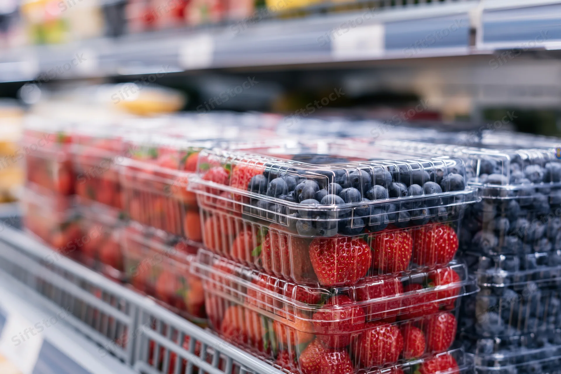 Rows of clear plastic clamshell containers filled with fresh blueberries and strawberries on a supermarket shelf