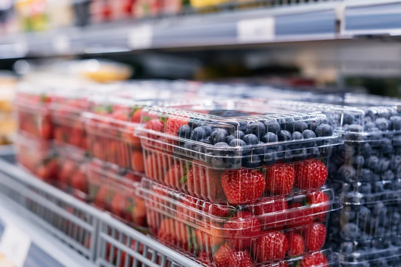 Rows of clear plastic clamshell containers filled with fresh blueberries and strawberries on a supermarket shelf