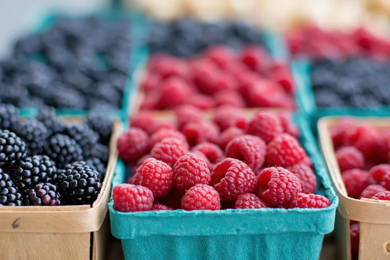Rows of fresh raspberries and blackberries in small cardboard containers at a market display