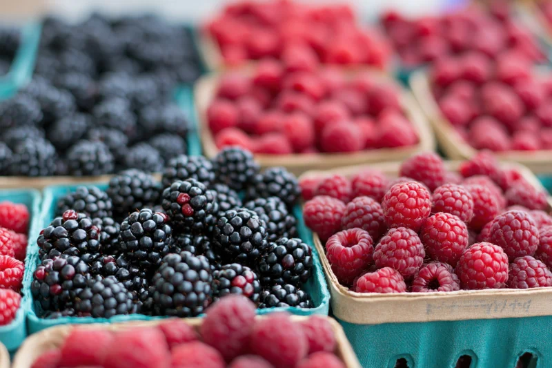 Rows of fresh blackberries and raspberries in teal baskets at a market stall