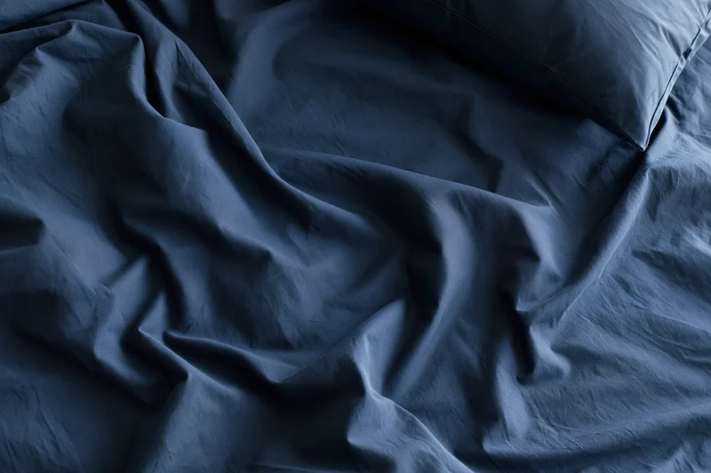 Rumpled navy blue sheets with a single pillow on a bed