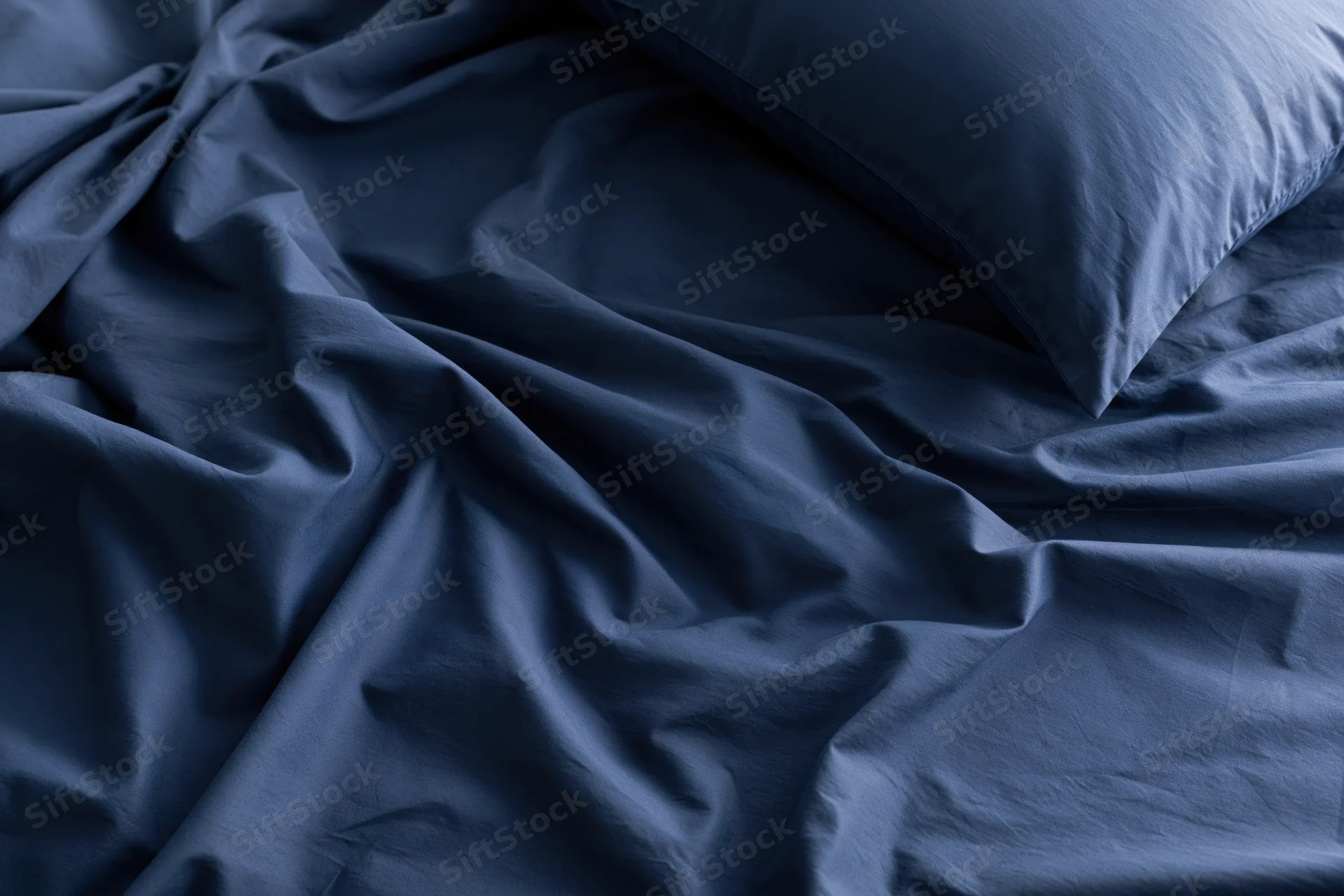 Rumpled dark navy blue sheets with a single pillow on a bed