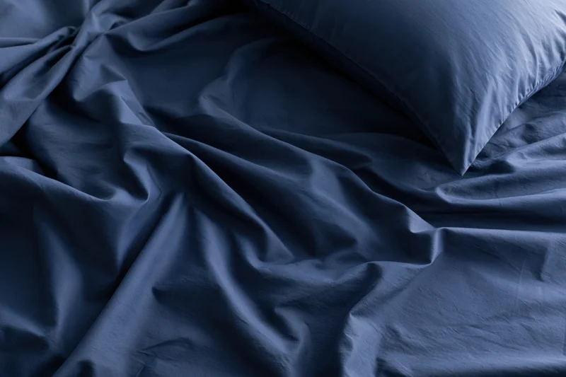 Rumpled dark navy blue sheets with a single pillow on a bed