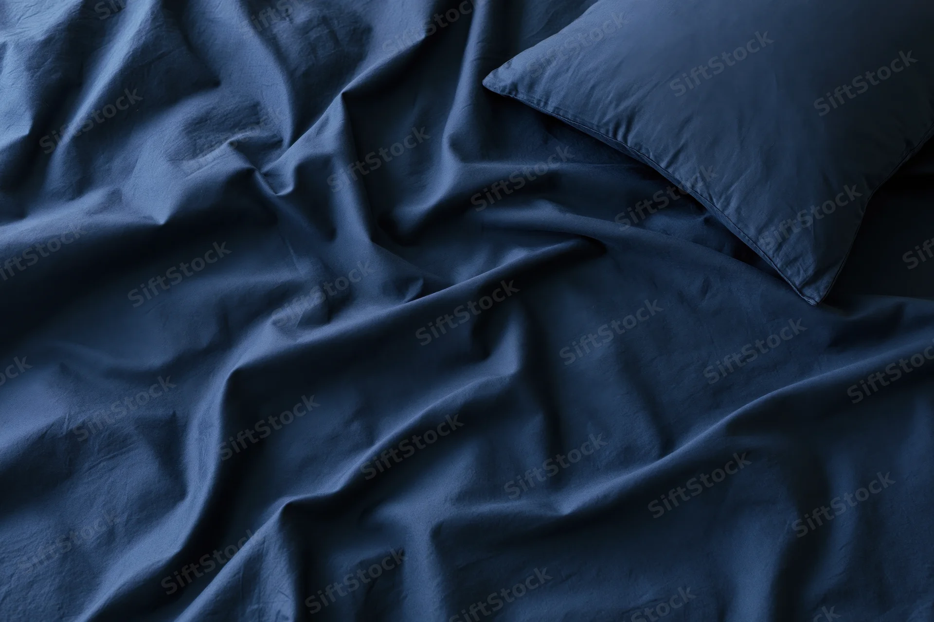 Rumpled dark navy blue sheets with a single pillow on a bed