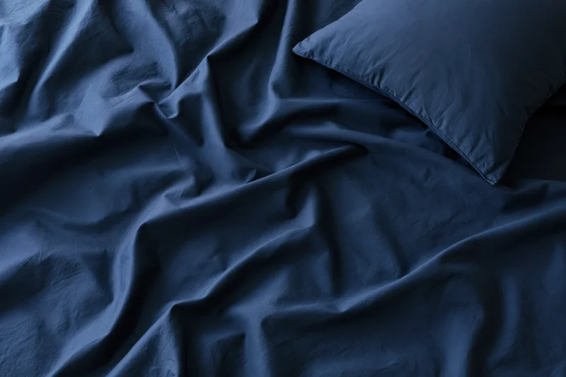 Rumpled dark navy blue sheets with a single pillow on a bed