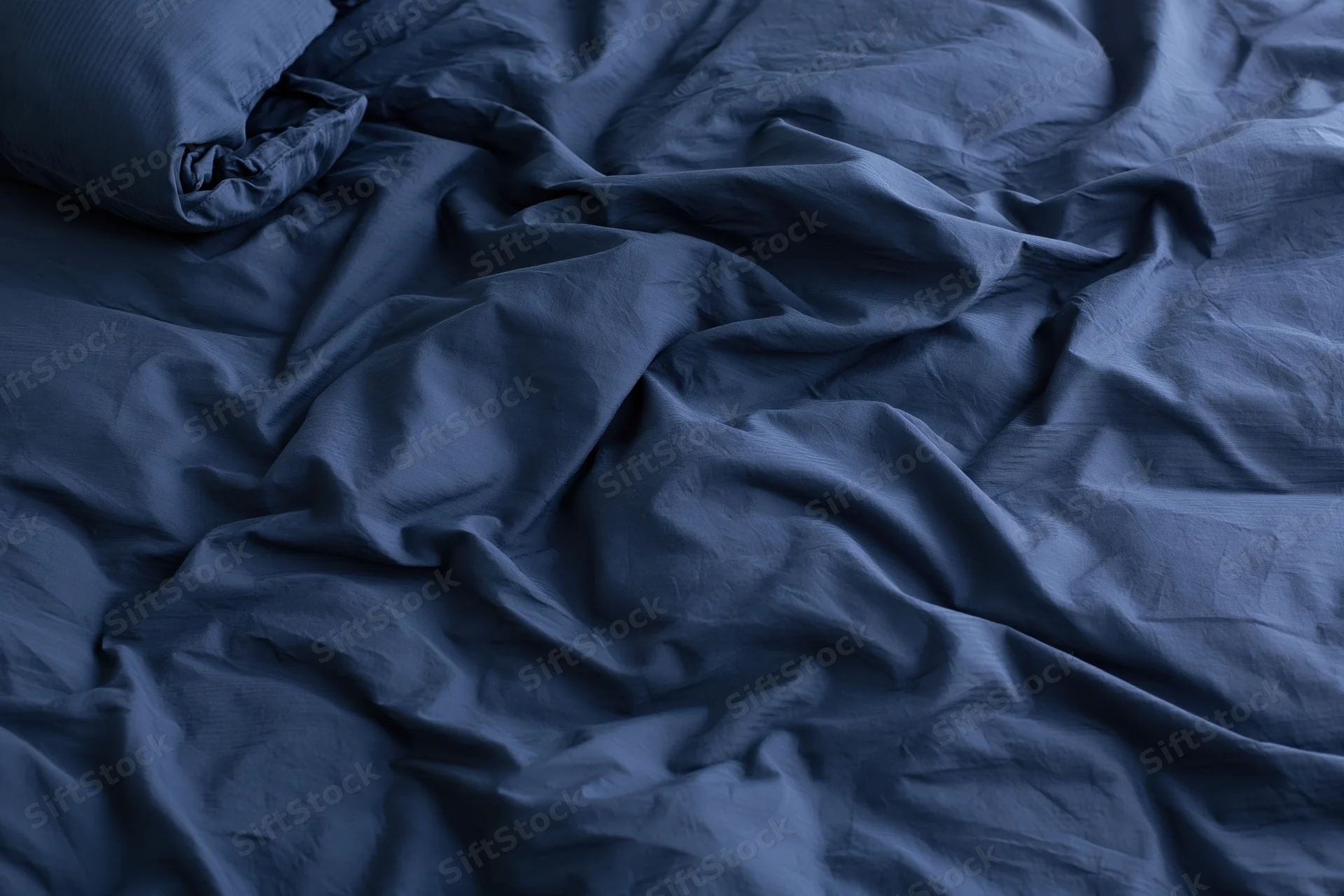 Rumpled navy blue duvet cover and pillow on a bed