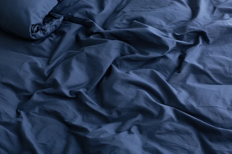 Rumpled navy blue duvet cover and pillow on a bed
