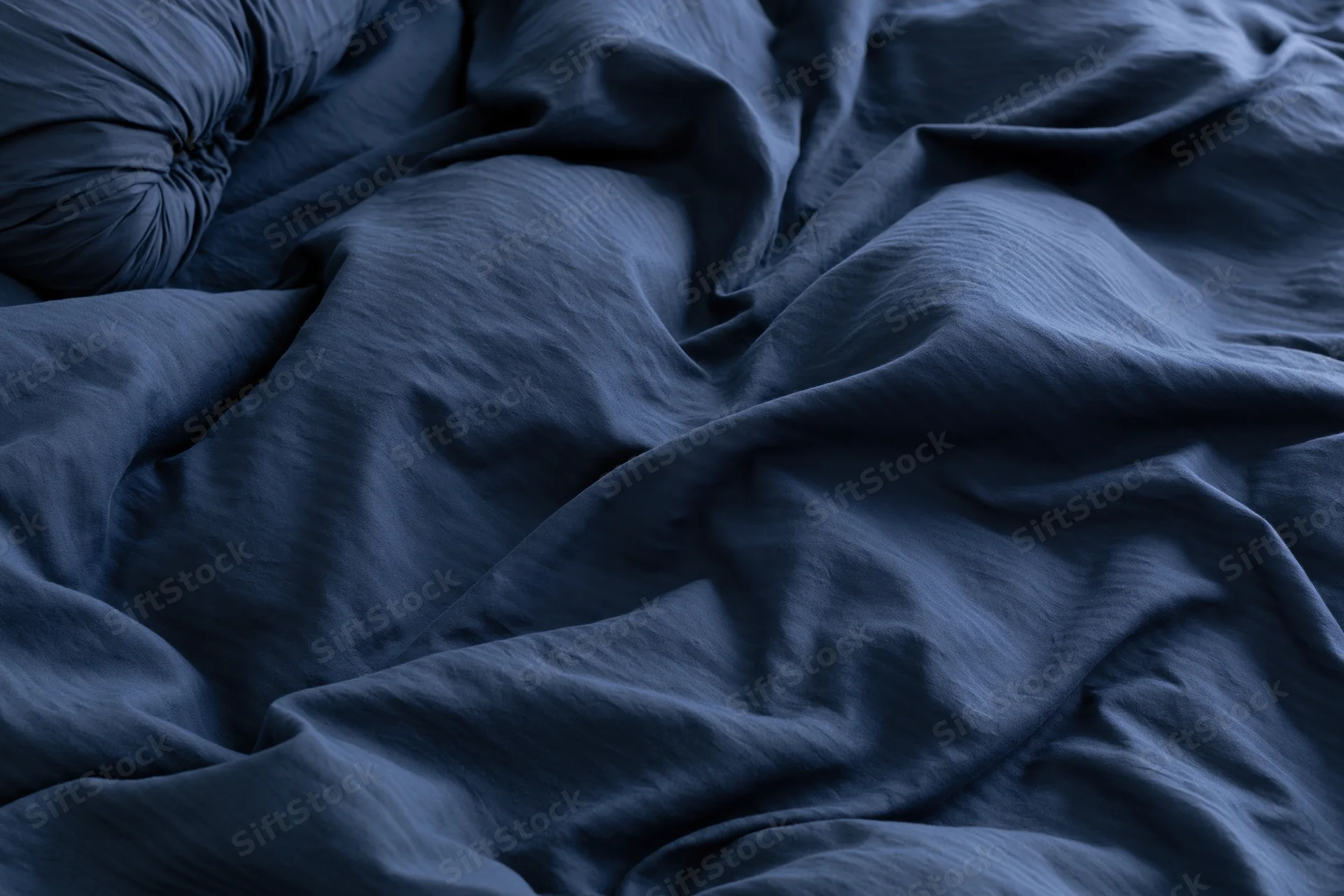 Rumpled navy blue duvet cover filling the frame with deep folds and shadows