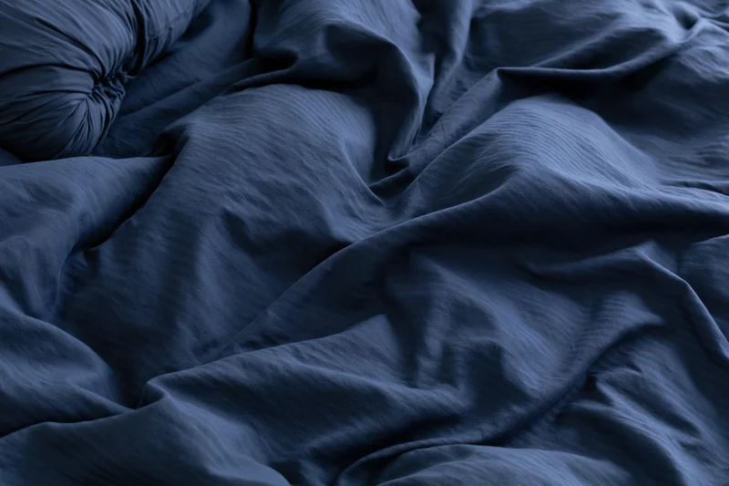 Rumpled navy blue duvet cover filling the frame with deep folds and shadows