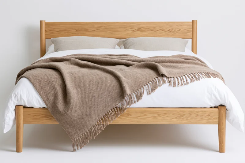 Wooden bed with white bedding and beige throw blanket in a minimalist bedroom setting