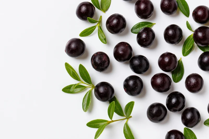 Acai berries and green leaves scattered on white surface