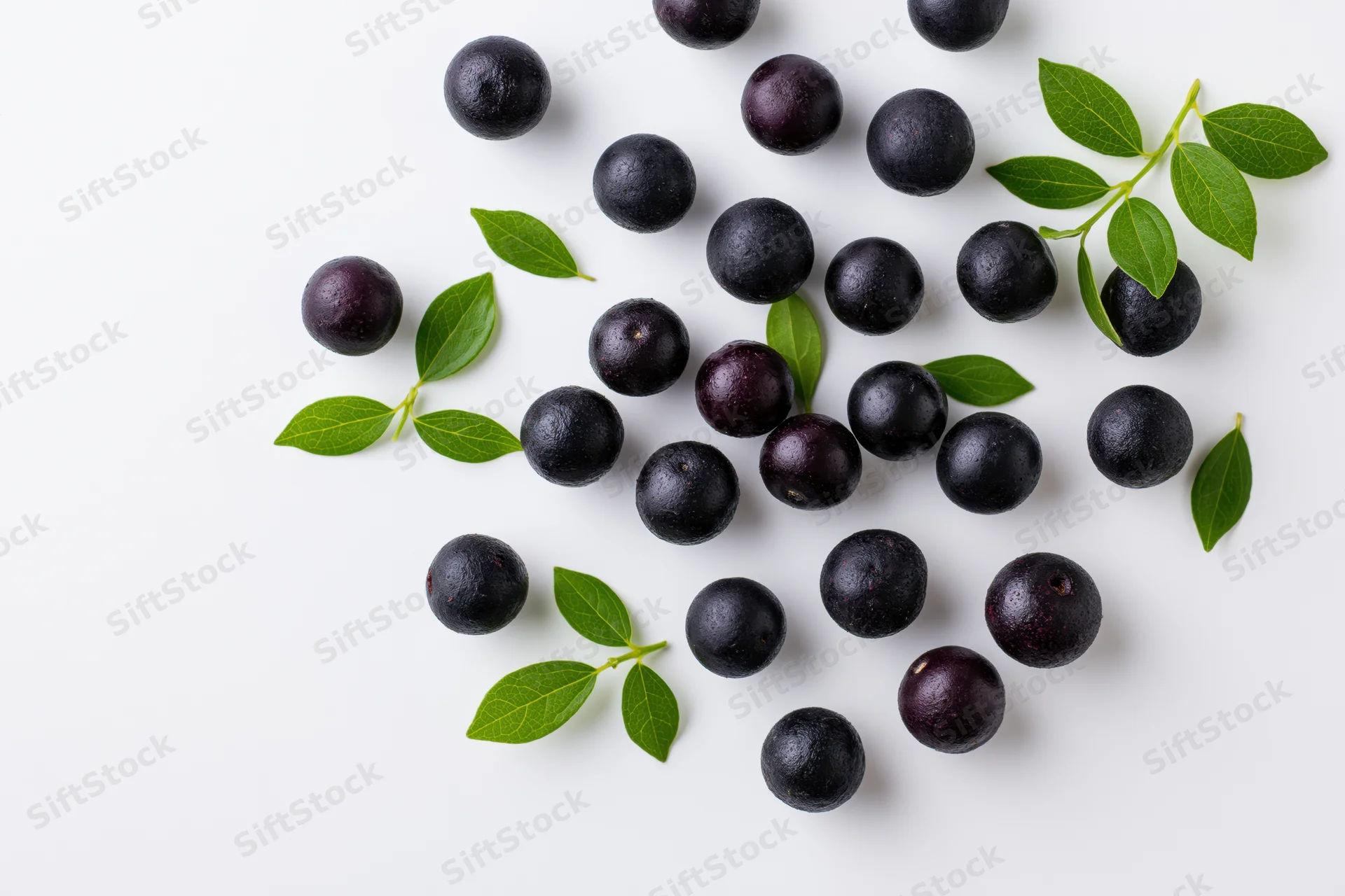 Scattered acai berries and green leaves on white surface