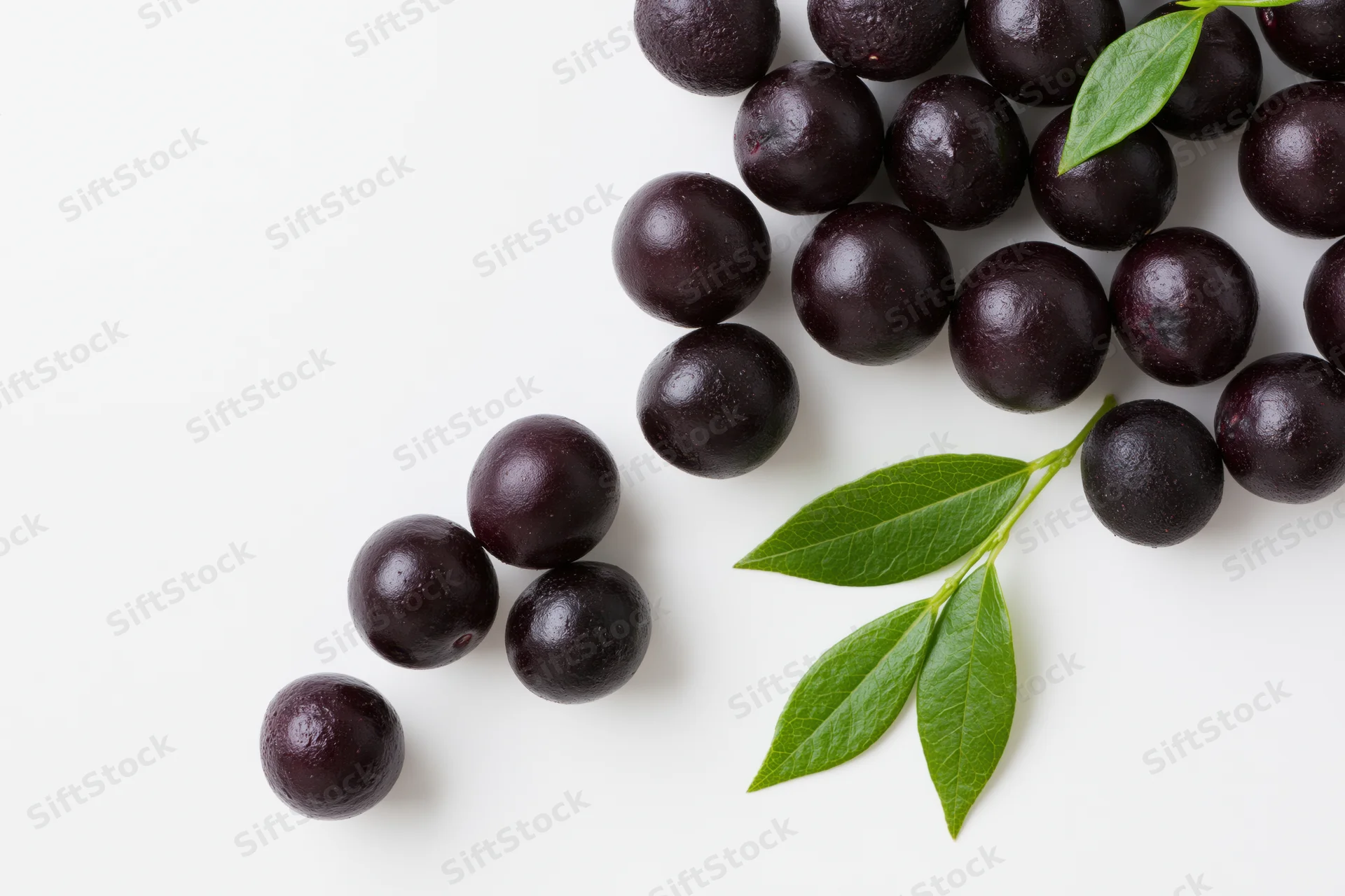 Scattered acai berries with green leaves on white background