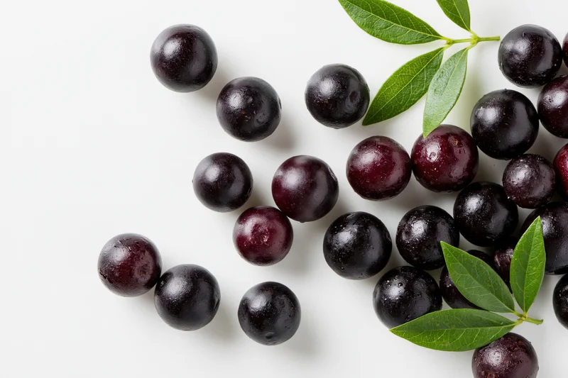 Scattered acai berries with green leaves on white background