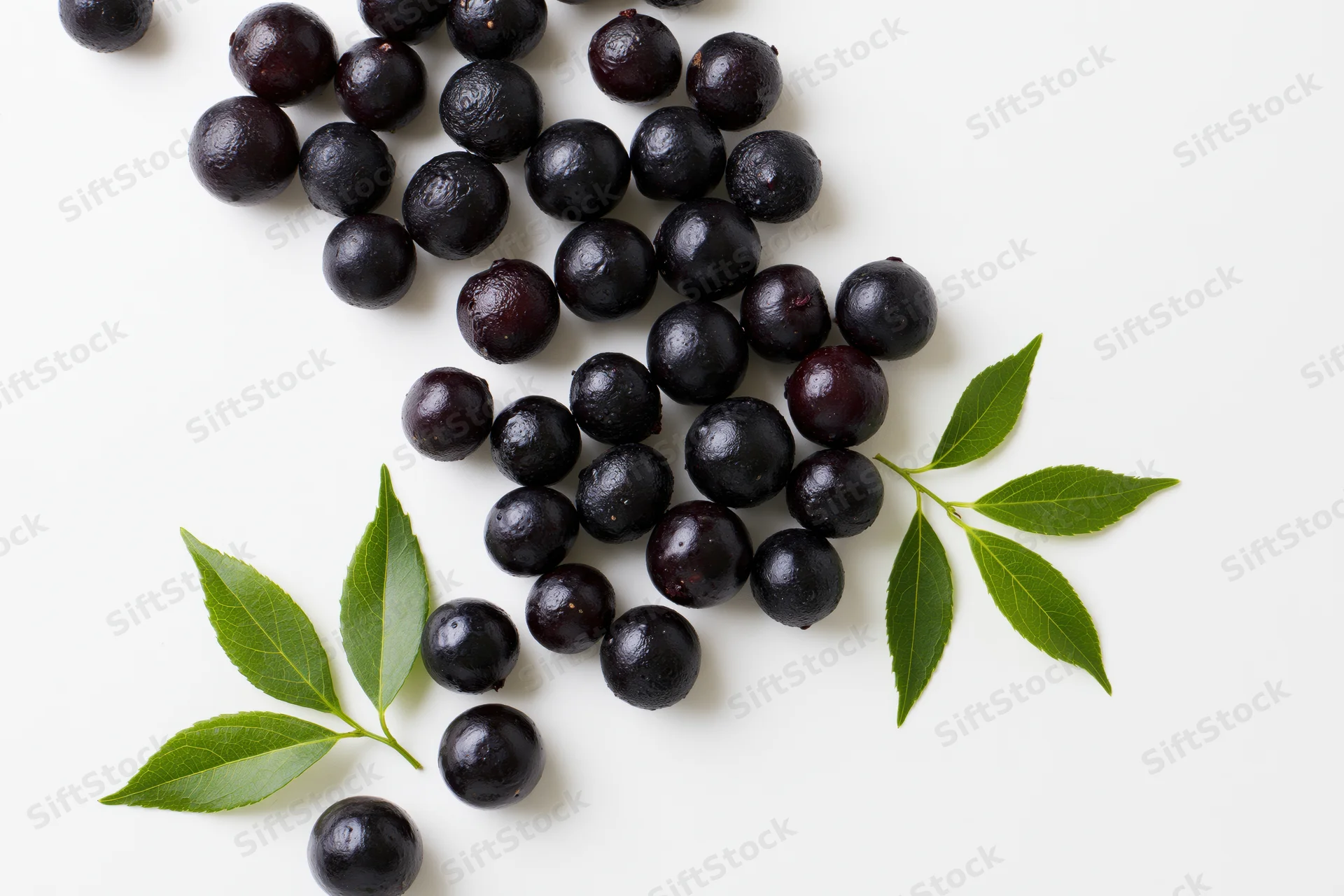 Scattered acai berries with fresh green leaves on white background