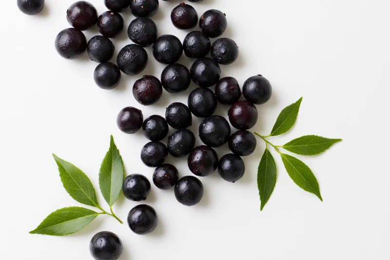 Scattered acai berries with fresh green leaves on white background