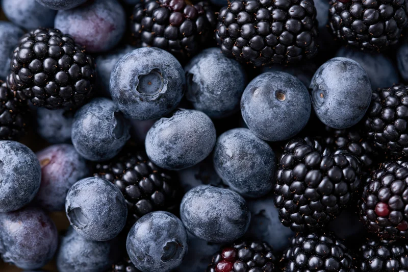 Closeup of scattered blueberries and blackberries piled together filling the frame