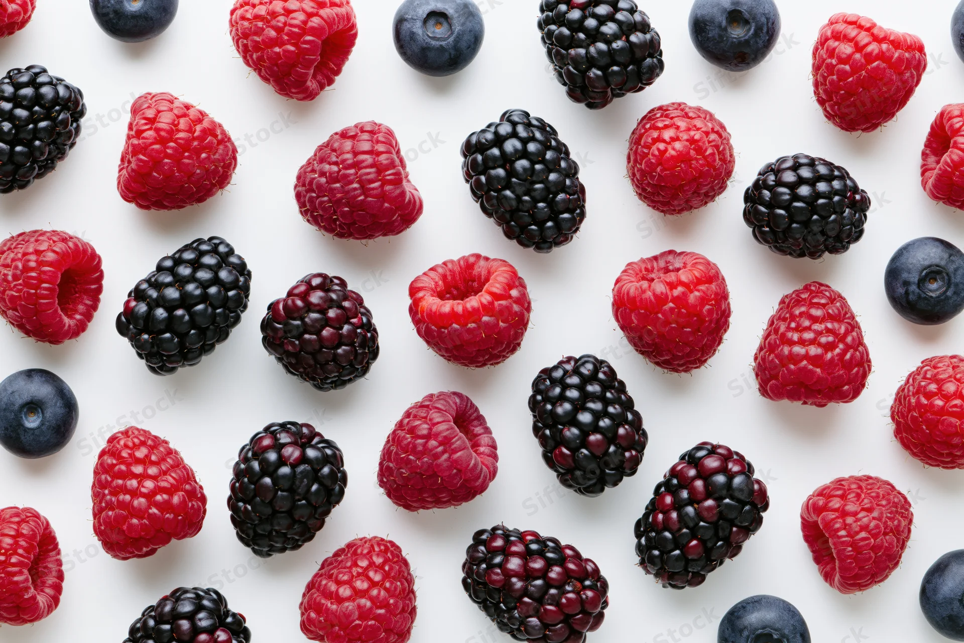 Scattered raspberries, blackberries and blueberries on white surface