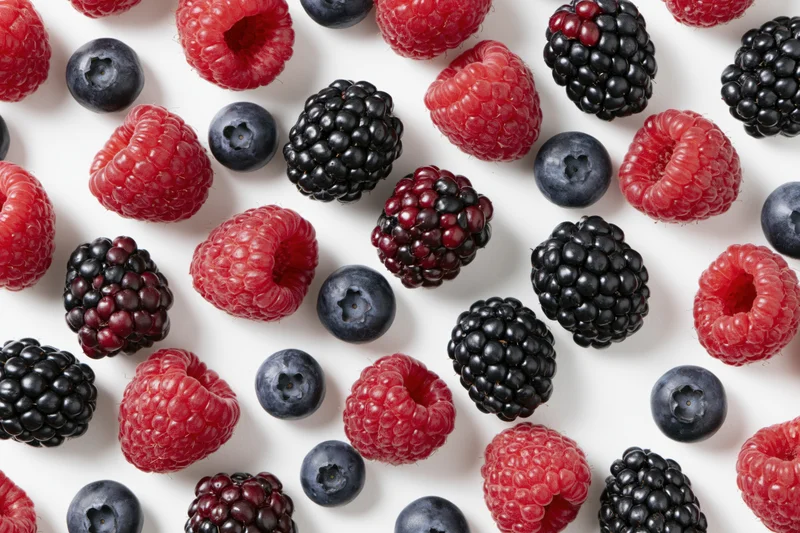 Scattered fresh raspberries blackberries and blueberries on white background