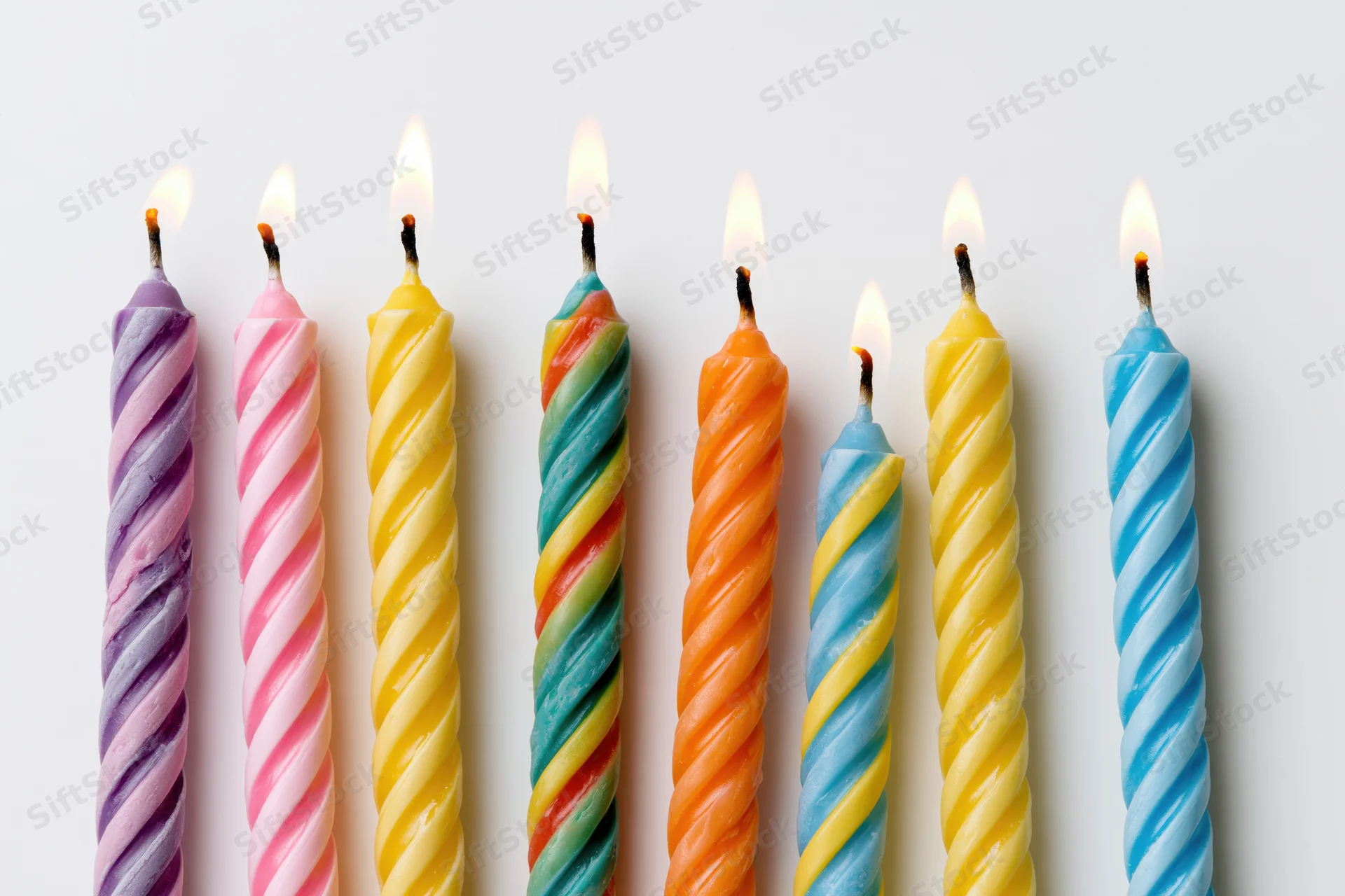 Seven lit colorful spiral candles in a row against a white background
