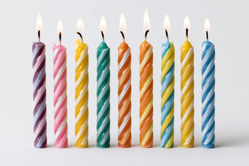 Seven lit colorful spiral candles in a row on white background