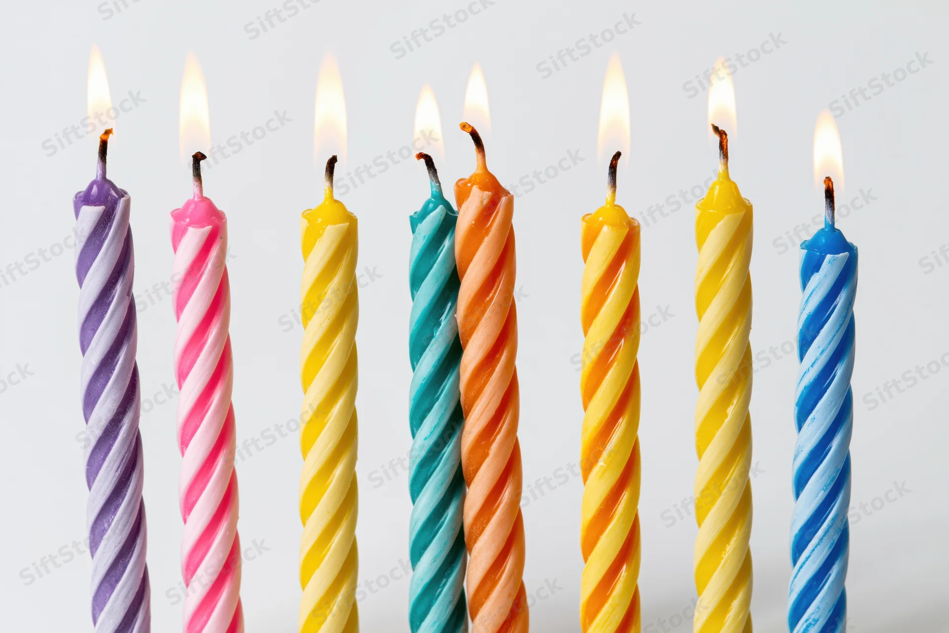 Seven lit colorful spiral birthday candles in a row against a white background