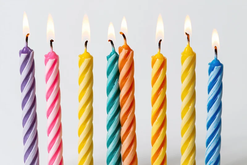 Seven lit colorful spiral birthday candles in a row against a white background