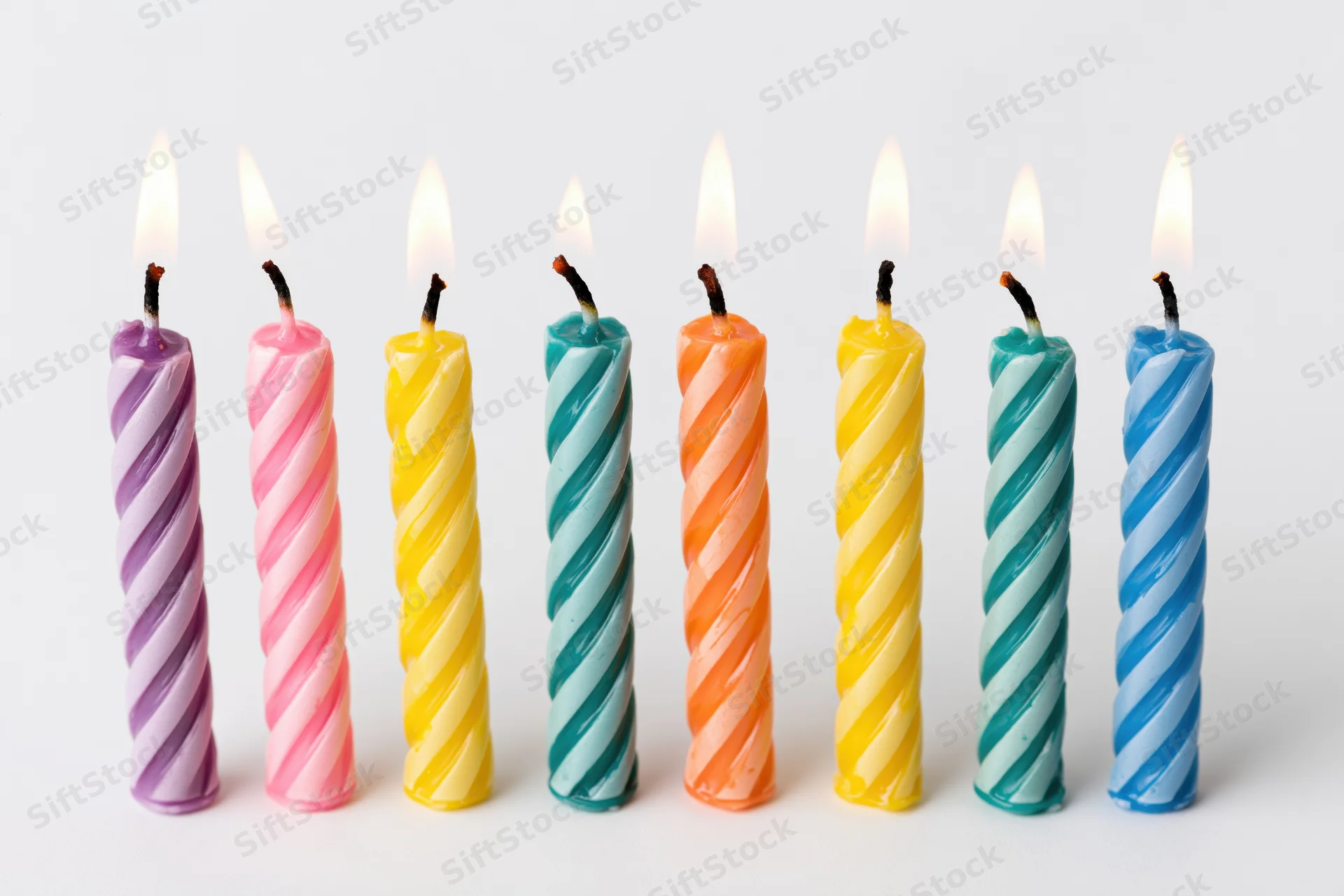 Seven lit colorful spiral candles in a row on white background