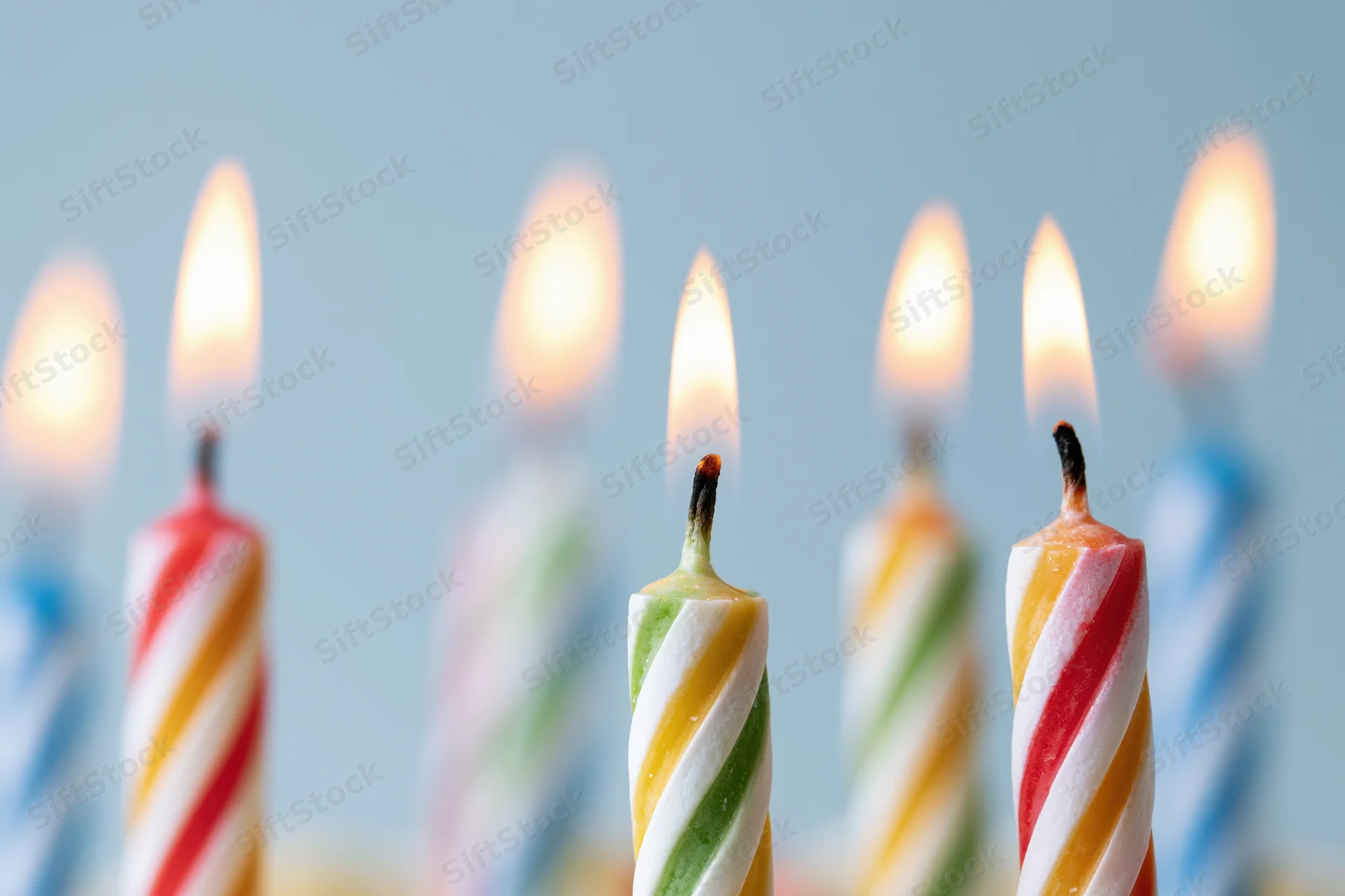 Lit birthday candles with spiral stripes arranged in a row against a soft blue background