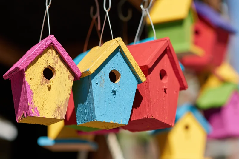 Colorful wooden birdhouses hanging from wire hooks outdoors
