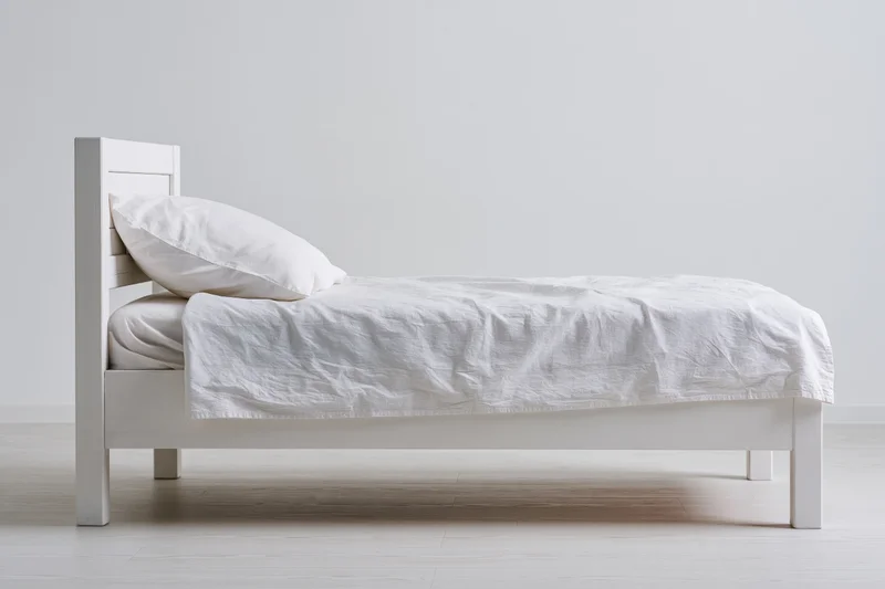 White wooden bed with rumpled white linen and pillow in minimalist bedroom