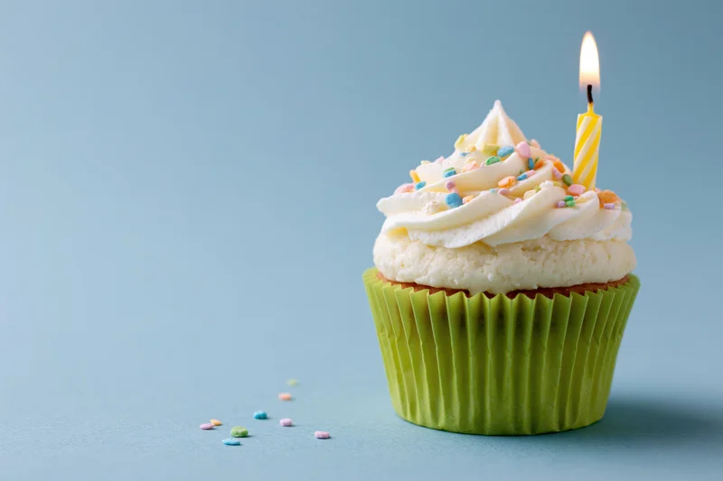 Single birthday cupcake with lit candle and sprinkles in lime green paper wrapper on blue background