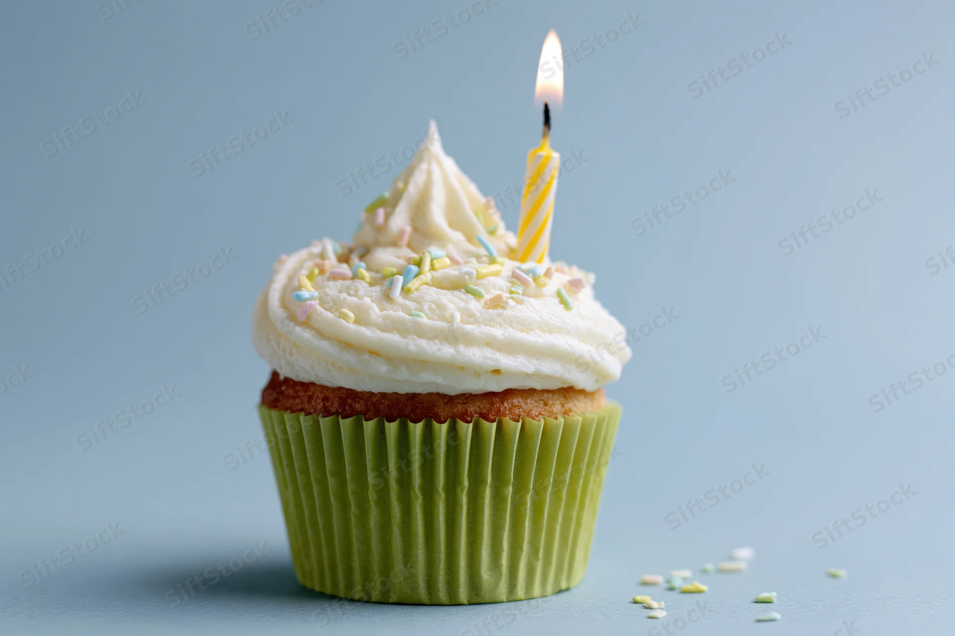 Single birthday cupcake with lit candle and sprinkles in lime green paper wrapper on blue surface